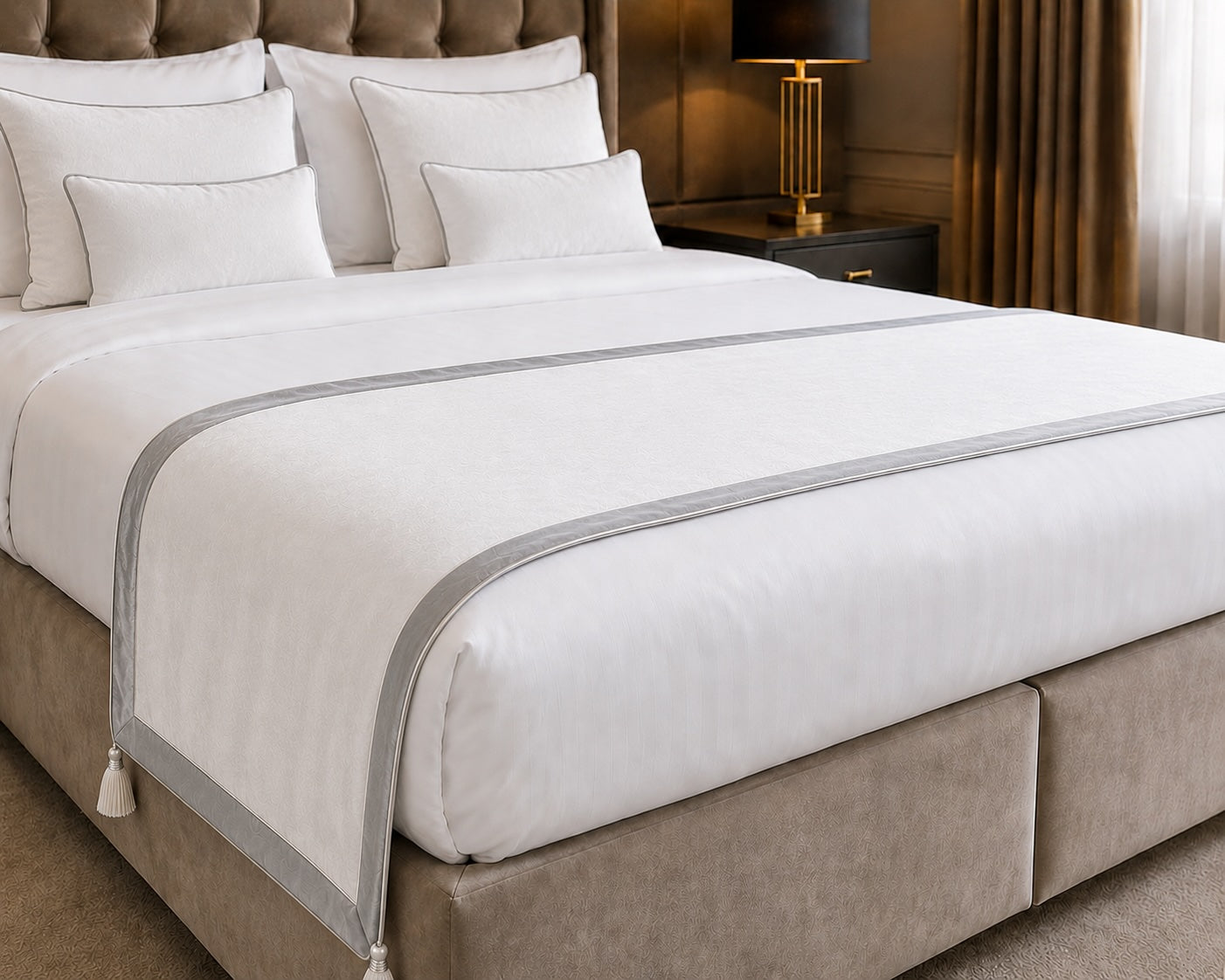 Eleganter Bettläufer in edlem Cremeweiß mit feiner silberner Paspelierung und dekorativen Quasten – eine stilvolle Ergänzung für luxuriöse Hotelzimmer, moderne Suiten und hochwertige Boxspringbetten.