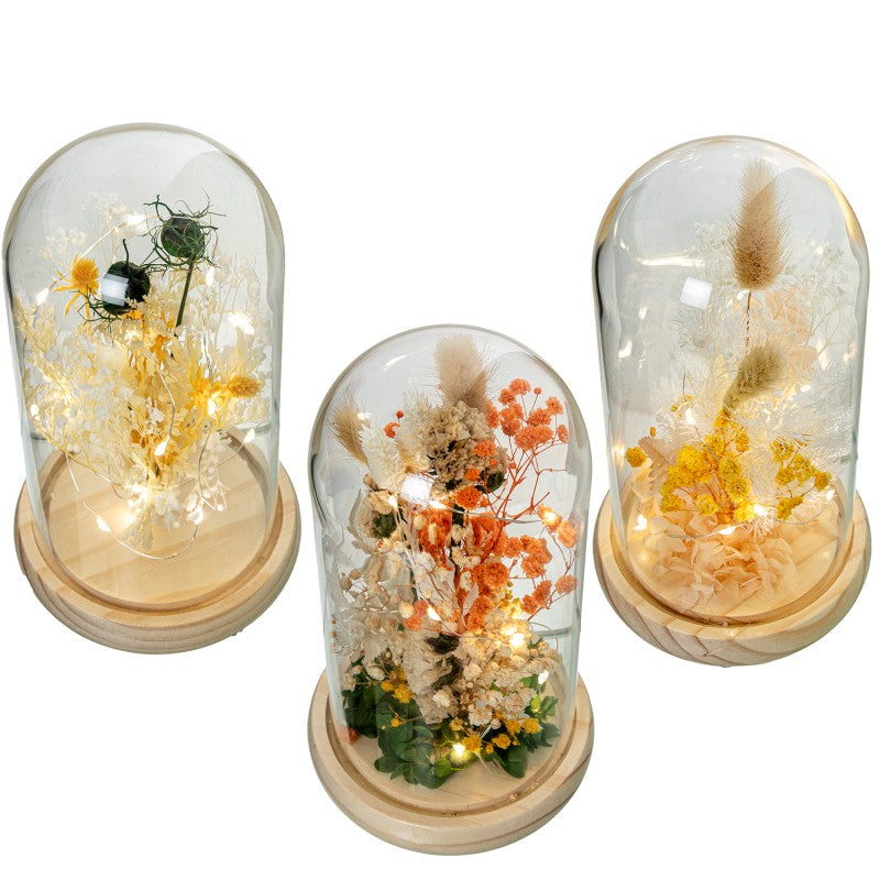 Die dekorative Glasglocke mit Holzsockel und künstlichen Blumenarrangements schafft eine stimmungsvolle und elegante Atmosphäre.
